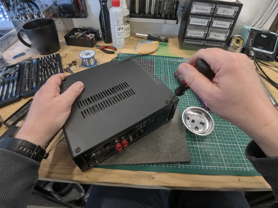 First-person view of hands unscrewing the case of an electronics unit on a repair bench.